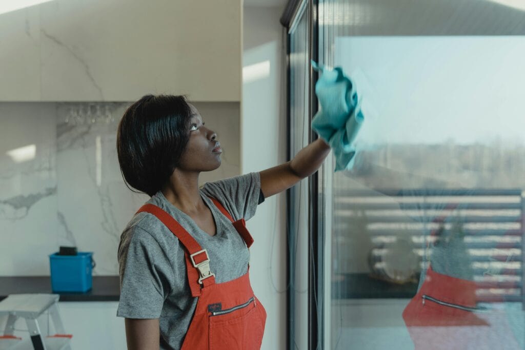 cleaning a window A woman in overalls cleans a glass window with a rag, emphasizing professional housekeeping.